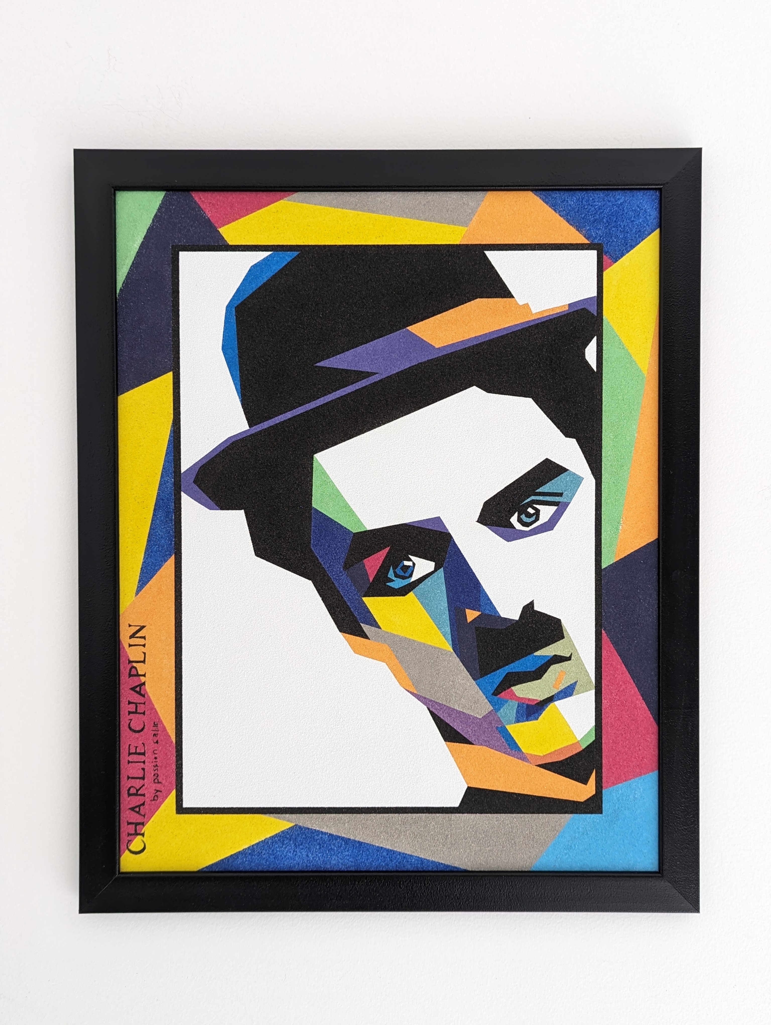 Portrait de Charlie Chaplin revisité dans un style graphique et coloré, entre formes géométriques et contrastes. Une création originale entièrement réalisée en sable.